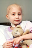 A beautiful little girl who has lost her hair due to chemotherapy. She is holding a teddy bear and a needle plunger.